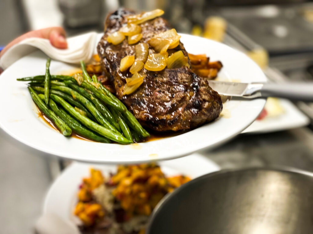 image of a steak with caramelized green beans and a side of green beans on a white plate
